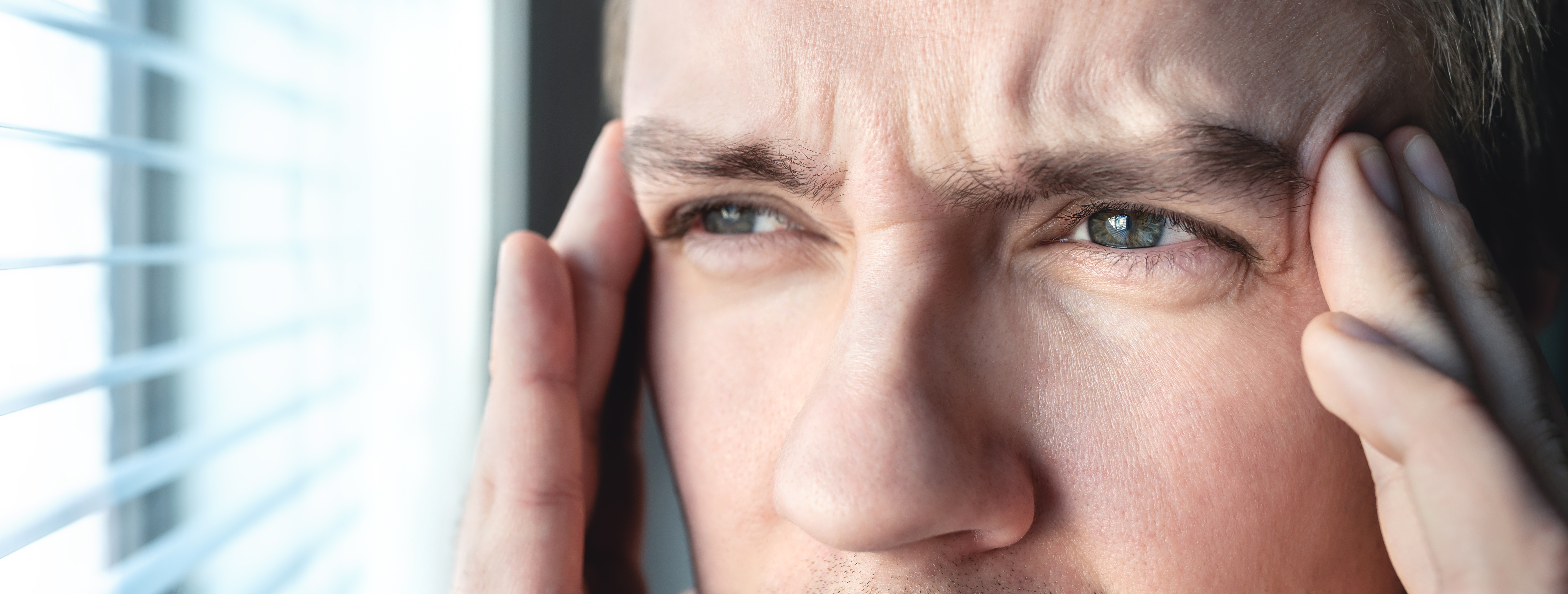 Nærbillede af en mand, der tager sig til sin tindinger og kigger ud af et vindue